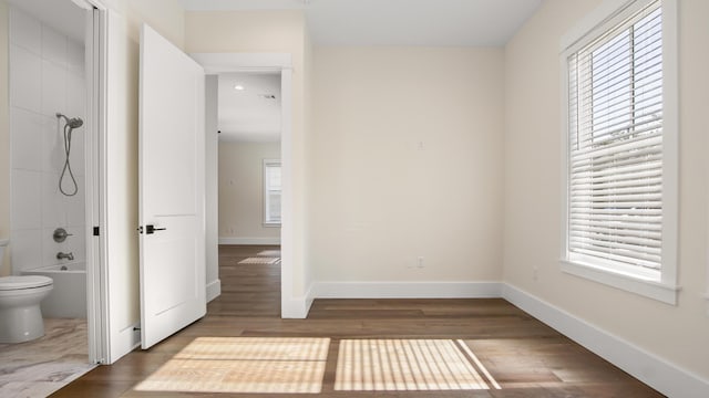 interior space with toilet, wood-type flooring, and bathing tub / shower combination