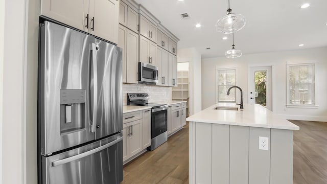 kitchen with gray cabinetry, sink, stainless steel appliances, pendant lighting, and a center island with sink