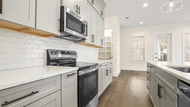 kitchen with stainless steel appliances, light stone counters, dark hardwood / wood-style flooring, backsplash, and pendant lighting