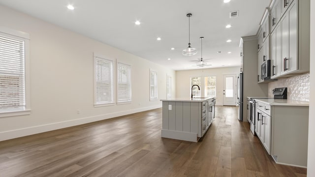 kitchen with decorative light fixtures, gray cabinets, a kitchen island with sink, and appliances with stainless steel finishes