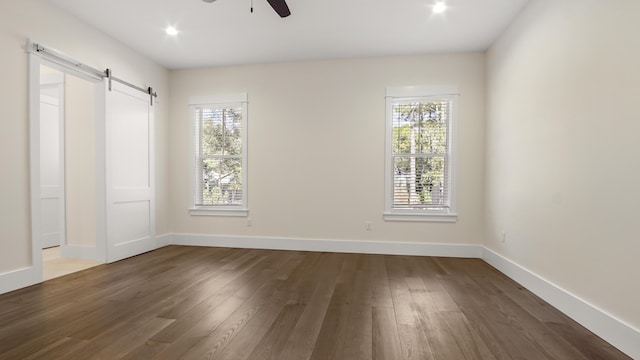 spare room featuring a barn door, ceiling fan, plenty of natural light, and dark hardwood / wood-style flooring