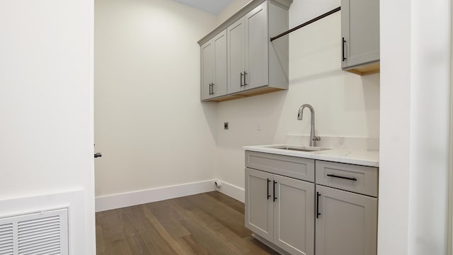 clothes washing area with electric dryer hookup, dark wood-type flooring, sink, and cabinets