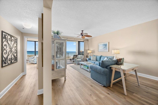 living room featuring a textured ceiling, a water view, light hardwood / wood-style flooring, and a wealth of natural light