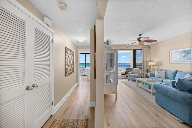 living room with a textured ceiling, a water view, ceiling fan, and light hardwood / wood-style floors