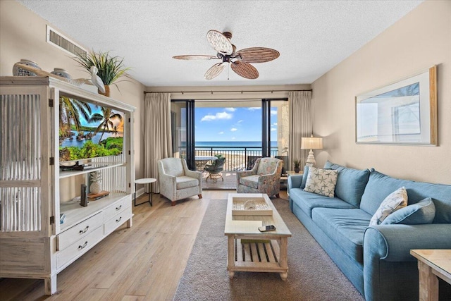 living room featuring ceiling fan, light hardwood / wood-style flooring, a water view, and a textured ceiling