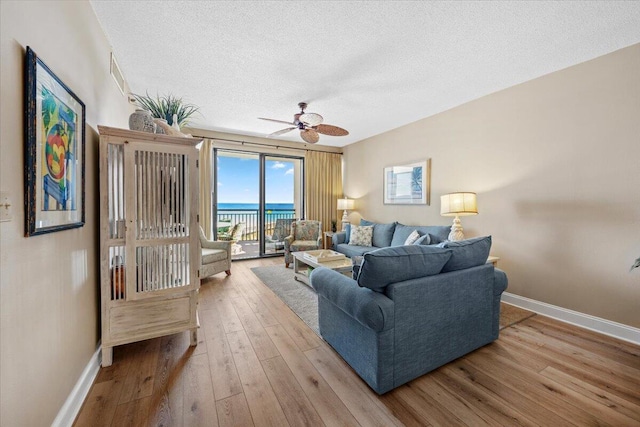 living room with ceiling fan, light hardwood / wood-style floors, a water view, and a textured ceiling