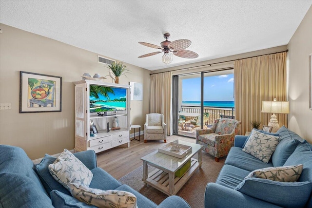 living room with a textured ceiling, a water view, light hardwood / wood-style flooring, and ceiling fan