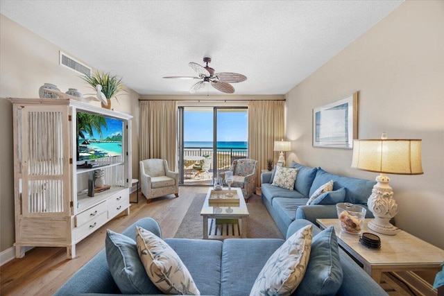 living room with ceiling fan, a textured ceiling, and light wood-type flooring