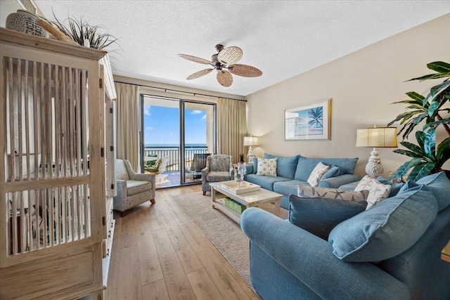 living room featuring ceiling fan, a water view, light wood-type flooring, and a textured ceiling