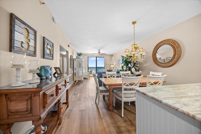 dining area featuring ceiling fan with notable chandelier, a textured ceiling, and hardwood / wood-style flooring