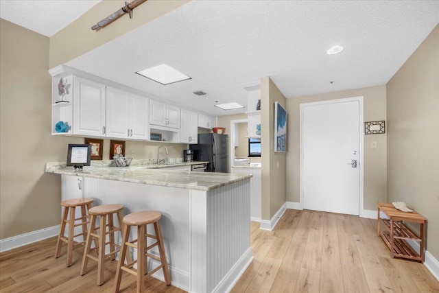 kitchen featuring white cabinets, black fridge, sink, a kitchen bar, and kitchen peninsula