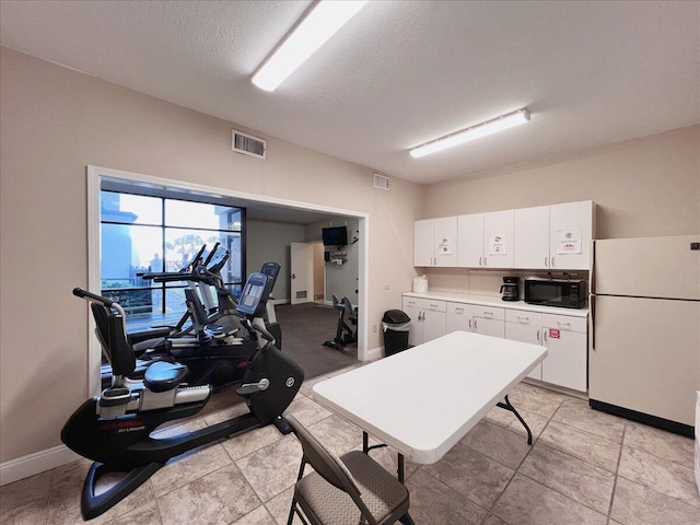 interior space with a textured ceiling, white refrigerator, and white cabinetry