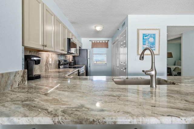 kitchen with light stone countertops, sink, backsplash, a textured ceiling, and appliances with stainless steel finishes