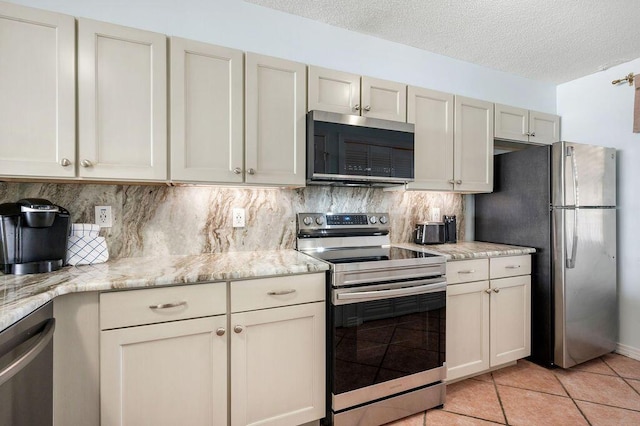 kitchen with decorative backsplash, appliances with stainless steel finishes, light tile patterned floors, and light stone counters