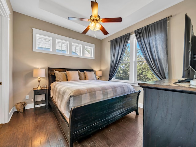 bedroom with a tray ceiling, ceiling fan, and dark wood-type flooring