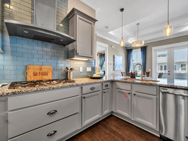 kitchen featuring tasteful backsplash, wall chimney exhaust hood, gray cabinetry, stainless steel appliances, and decorative light fixtures