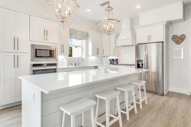 kitchen featuring a center island, premium range hood, white cabinetry, stainless steel appliances, and a chandelier