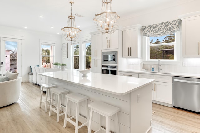 kitchen with white cabinetry, a center island, sink, stainless steel appliances, and pendant lighting