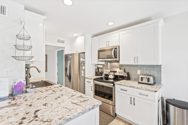 kitchen featuring backsplash, white cabinets, sink, light stone countertops, and appliances with stainless steel finishes