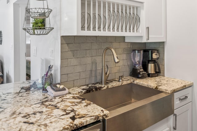 kitchen with white cabinets, backsplash, light stone counters, and sink