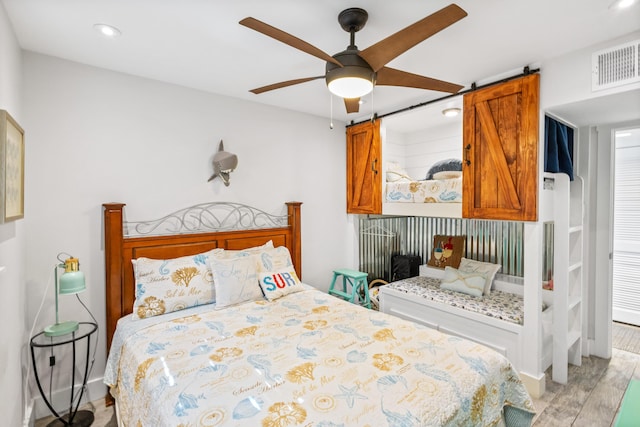 bedroom with a barn door, ceiling fan, and light hardwood / wood-style flooring