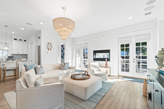 living room with a notable chandelier, light hardwood / wood-style flooring, and french doors