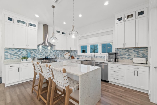 kitchen with appliances with stainless steel finishes, a kitchen island, sink, wall chimney range hood, and white cabinetry