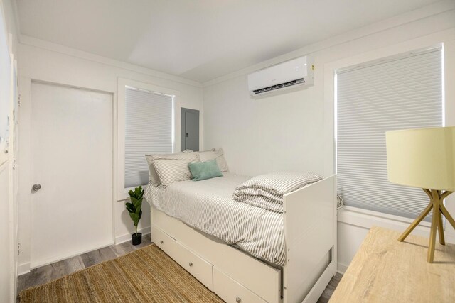 bedroom with electric panel, wood-type flooring, a wall mounted air conditioner, and ornamental molding