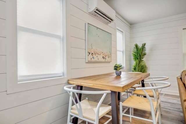 dining room with hardwood / wood-style floors, a wall mounted AC, a healthy amount of sunlight, and wood walls