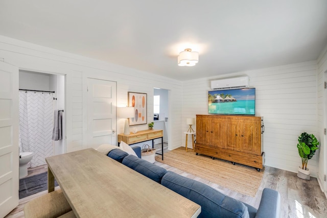 living room featuring a wall unit AC, wooden walls, and light hardwood / wood-style floors