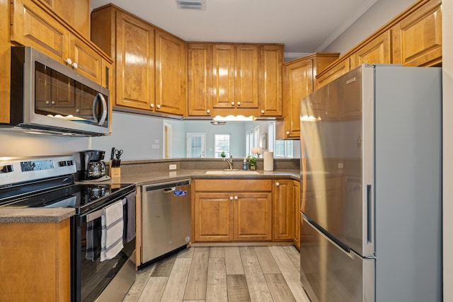 kitchen featuring light wood-type flooring, stainless steel appliances, ornamental molding, and sink