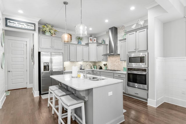 kitchen with appliances with stainless steel finishes, a breakfast bar, sink, wall chimney range hood, and a center island with sink