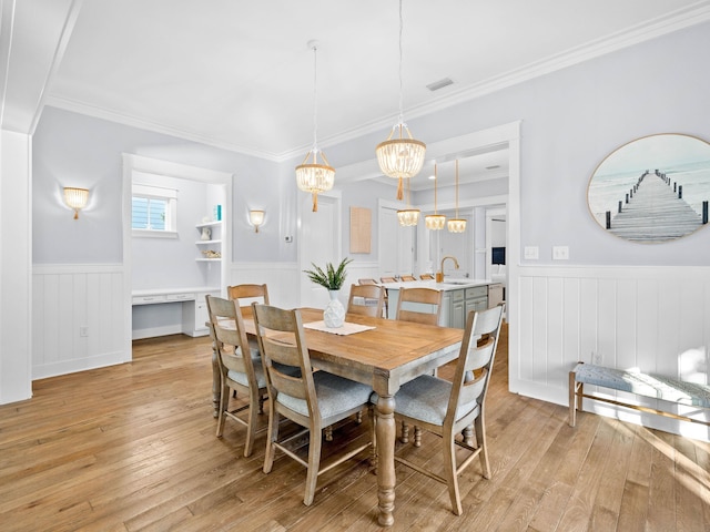 dining area with light hardwood / wood-style flooring, an inviting chandelier, ornamental molding, and sink