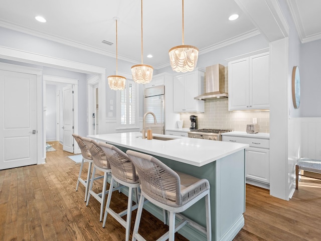 kitchen with white cabinets, pendant lighting, wall chimney range hood, and an island with sink