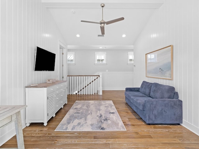 living room with ceiling fan, lofted ceiling with beams, and light wood-type flooring