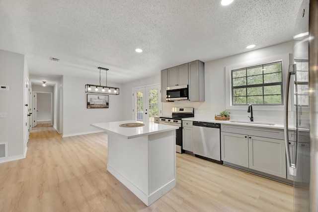 kitchen with gray cabinets, a kitchen island, appliances with stainless steel finishes, decorative light fixtures, and sink