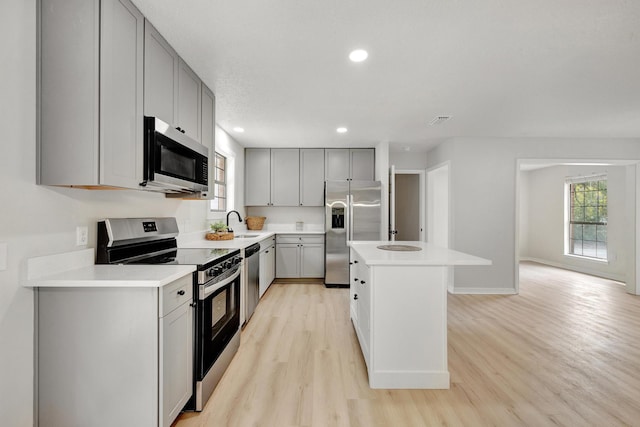 kitchen with sink, gray cabinets, stainless steel appliances, and a center island with sink