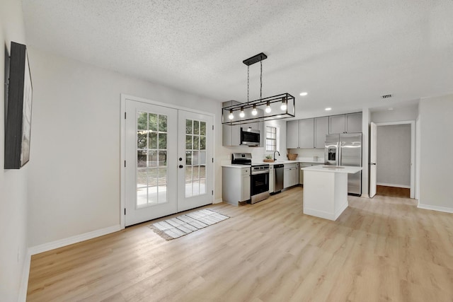 kitchen with french doors, a center island, hanging light fixtures, light hardwood / wood-style flooring, and appliances with stainless steel finishes