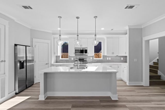 kitchen featuring light countertops, appliances with stainless steel finishes, an island with sink, and visible vents