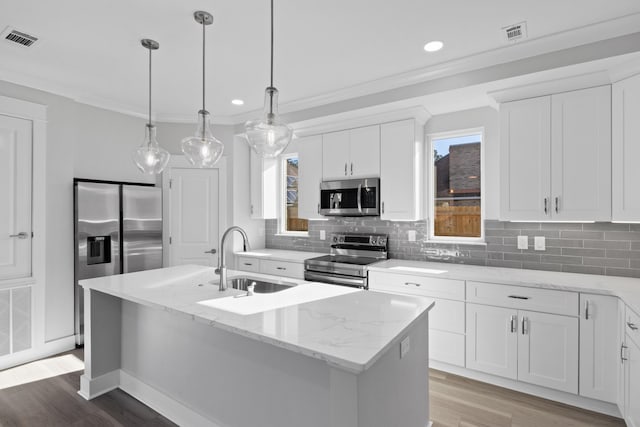 kitchen featuring light stone countertops, appliances with stainless steel finishes, a kitchen island with sink, sink, and white cabinetry