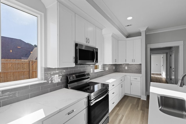 kitchen with white cabinets, sink, light stone countertops, ornamental molding, and appliances with stainless steel finishes