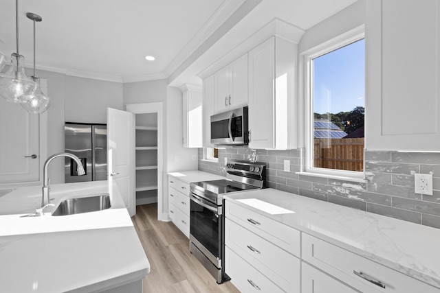 kitchen with light wood-style flooring, stainless steel appliances, a sink, ornamental molding, and backsplash