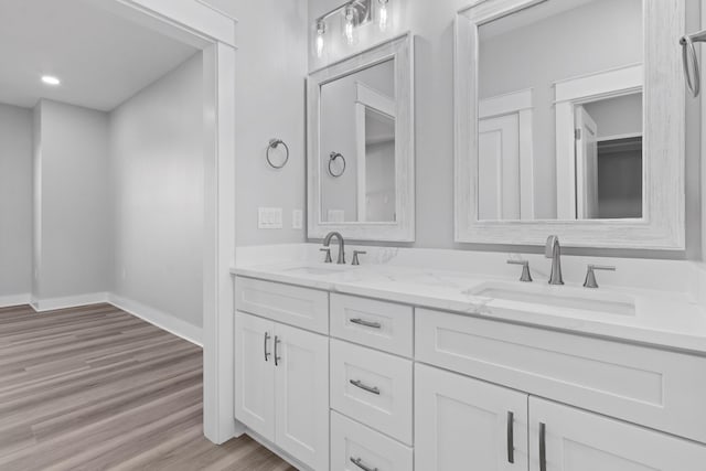 bathroom featuring double vanity, baseboards, a sink, and wood finished floors