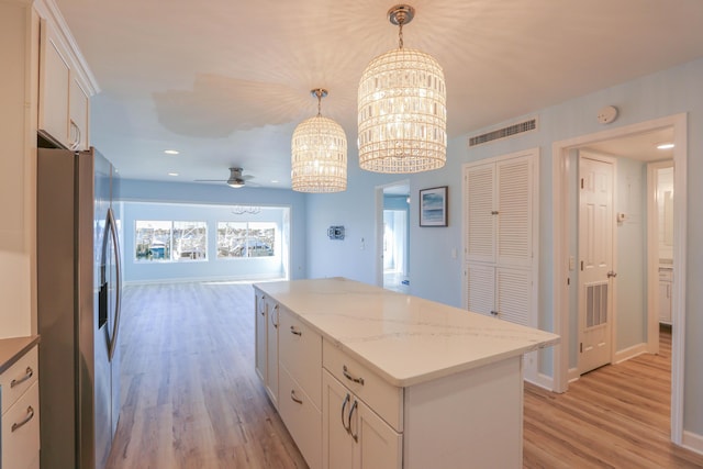 kitchen featuring white cabinets, stainless steel fridge, a kitchen island, and hanging light fixtures