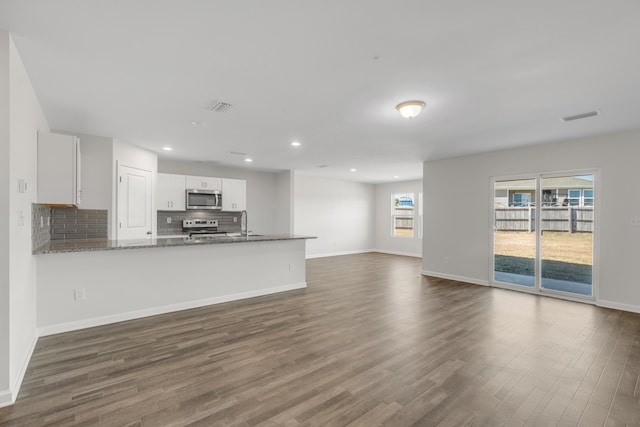 interior space featuring kitchen peninsula, tasteful backsplash, dark stone counters, stainless steel appliances, and white cabinetry