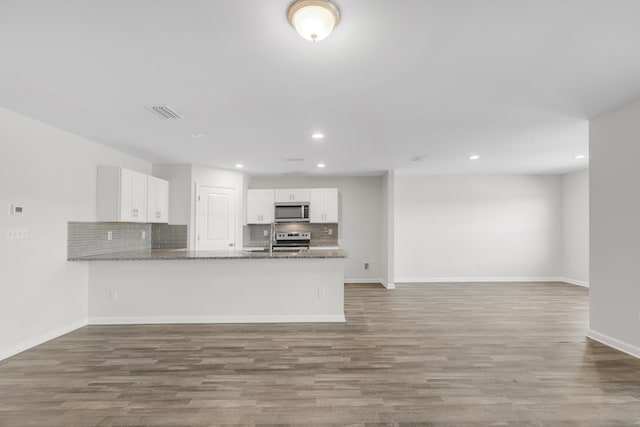 kitchen featuring kitchen peninsula, light wood-type flooring, dark stone counters, stainless steel appliances, and white cabinets