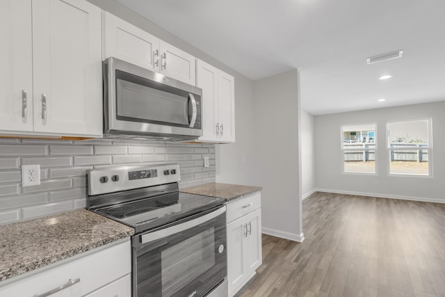 kitchen with stone counters, white cabinetry, stainless steel appliances, light hardwood / wood-style flooring, and decorative backsplash