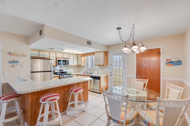 kitchen featuring sink, a notable chandelier, kitchen peninsula, light tile patterned floors, and appliances with stainless steel finishes