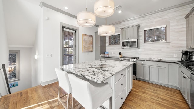 kitchen featuring gray cabinetry, decorative light fixtures, decorative backsplash, a kitchen island, and appliances with stainless steel finishes