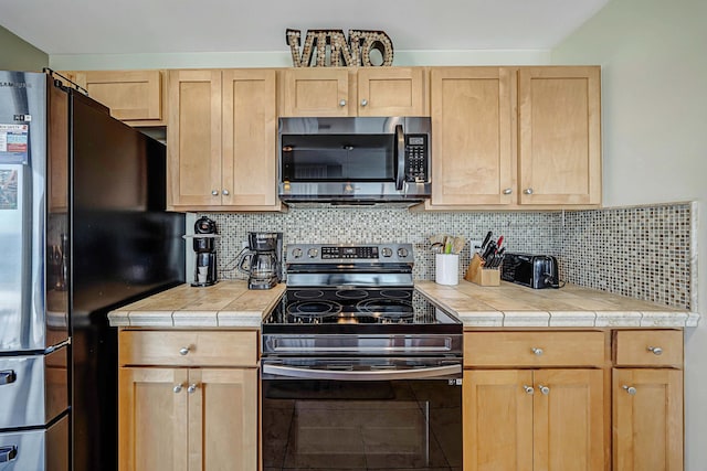 kitchen with light brown cabinetry, decorative backsplash, tile counters, and appliances with stainless steel finishes